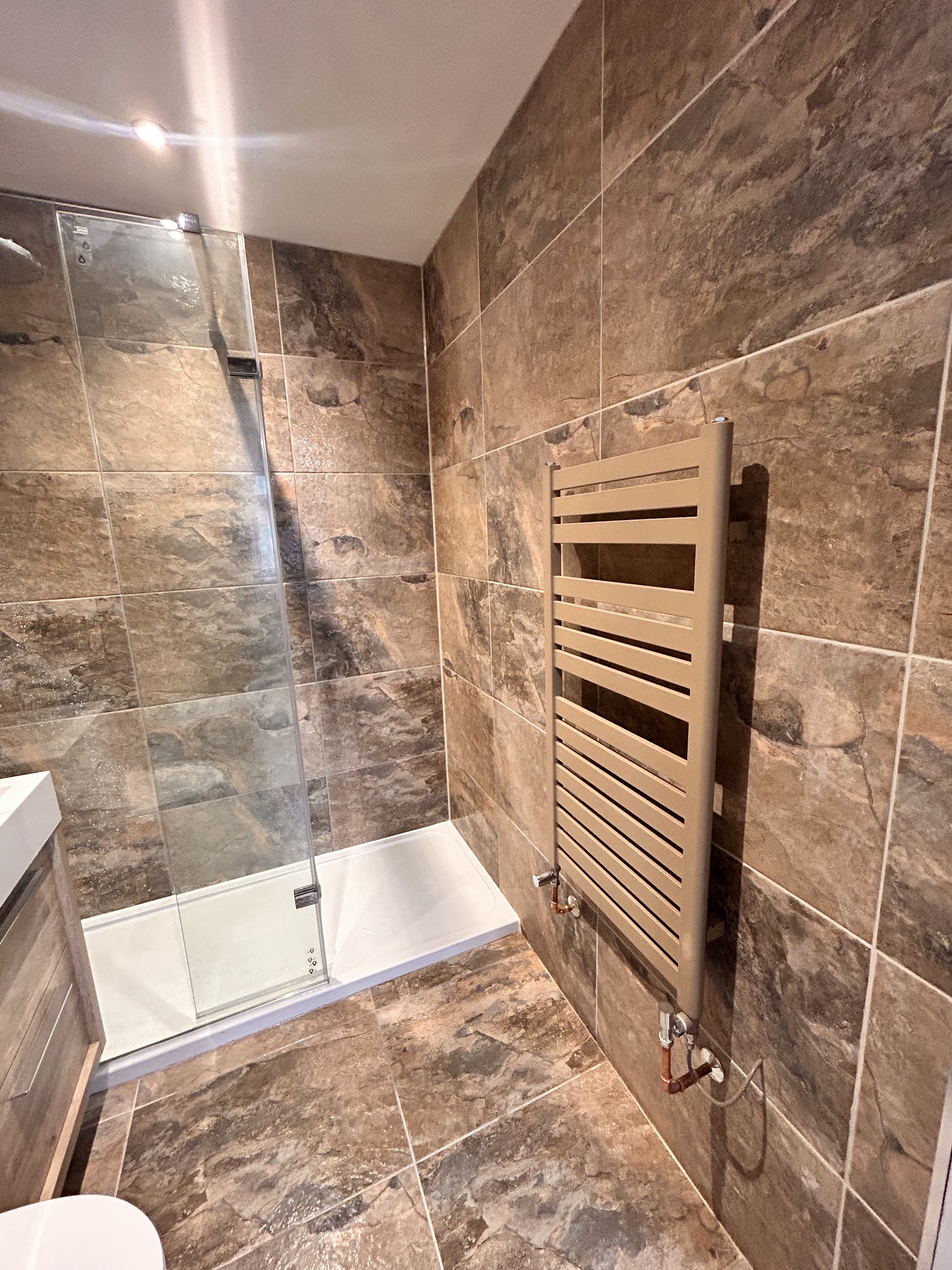 Walk-in shower with large stone-effect tiles and a bronze towel rail