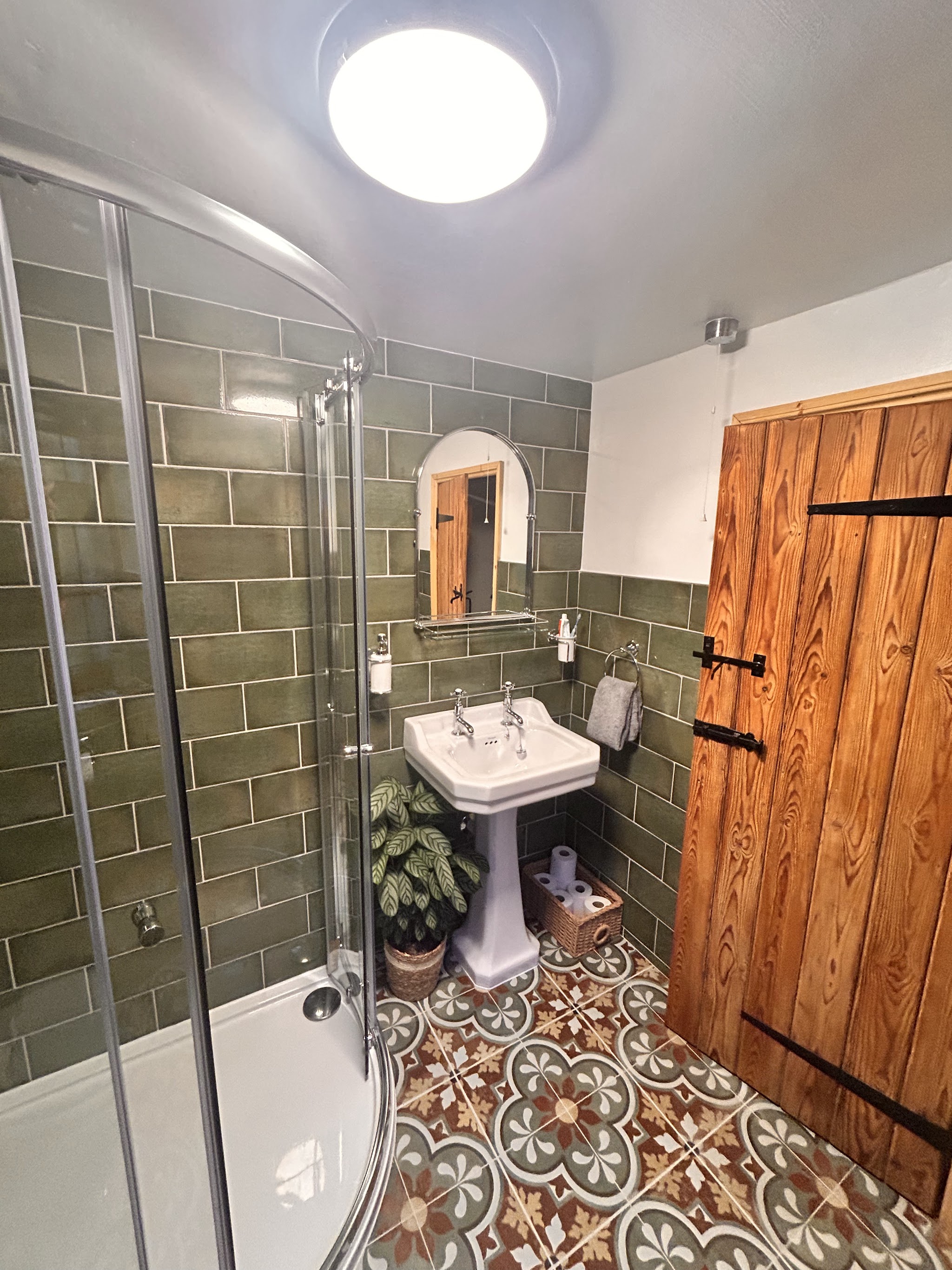 Cottage bathroom with sage metro tiles, patterned floor tiles and a pedestal basin