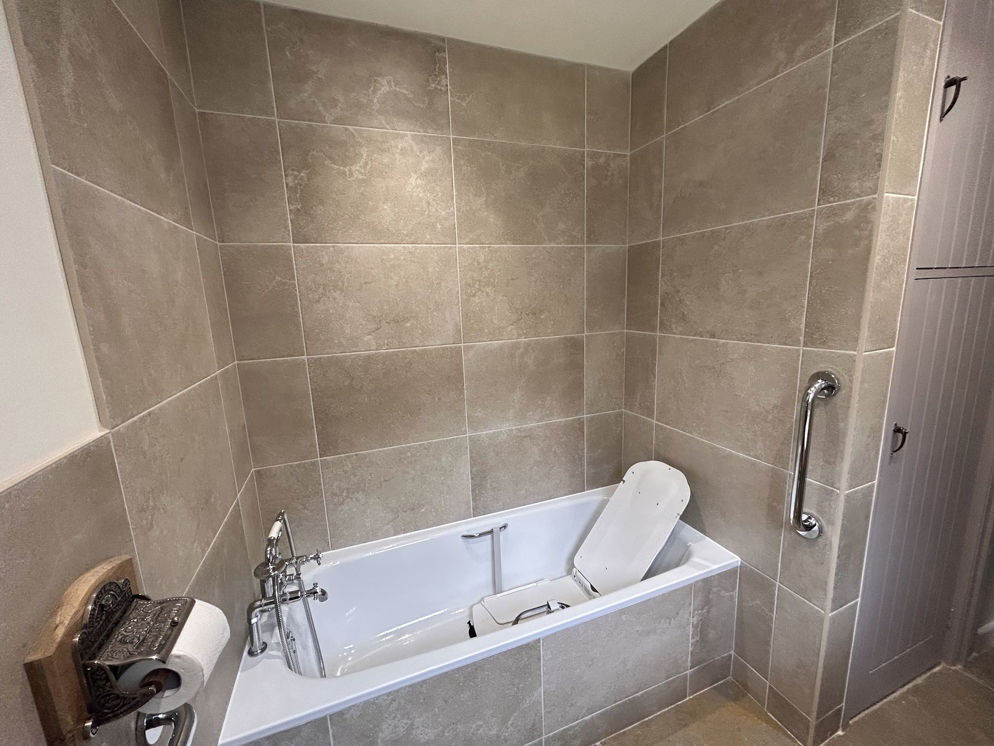 Tiled bathroom with a bath, grab rail and bath lift