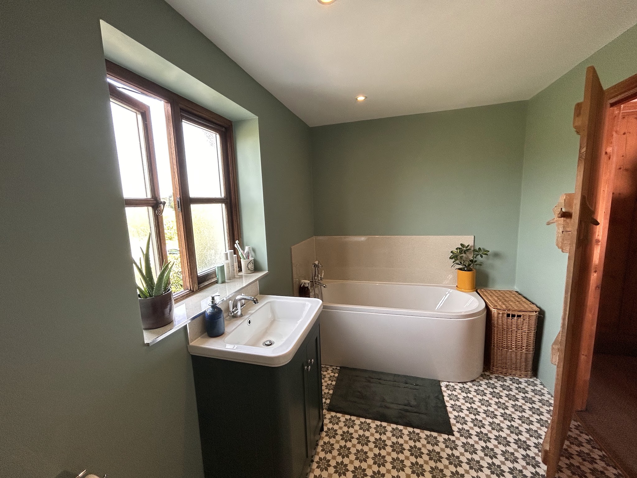 Green bathroom with a bath, a dark vanity unit and patterned floor tiles